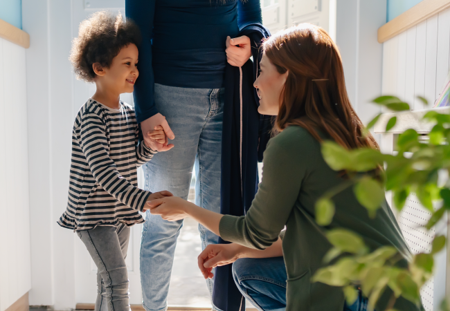 Transitions - Photograph of an Early Years educator greeting a child and her parent.
